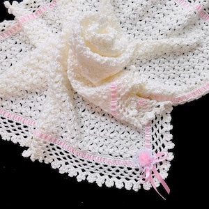 May include: White crocheted baby blanket with a pink satin ribbon border and a pink satin bow with a white crocheted flower.