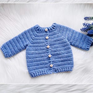 May include: A blue crocheted baby cardigan with wooden buttons.