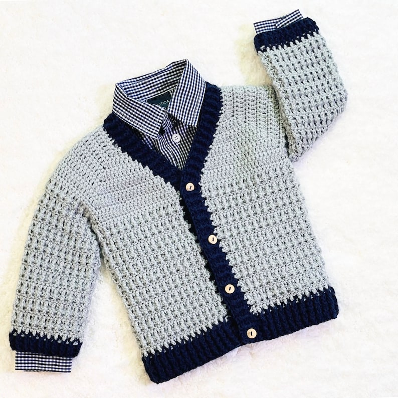 May include: A gray and navy blue crocheted cardigan with a button closure. The cardigan has a V-neck and a textured stitch pattern.