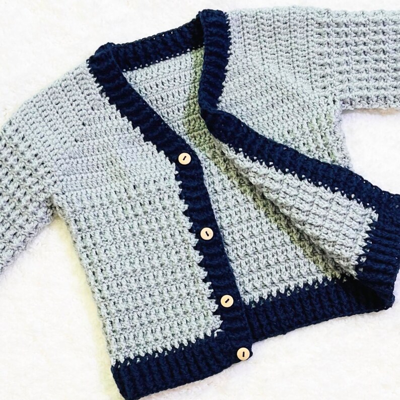 May include: A gray crocheted cardigan with a navy blue trim and wooden buttons.