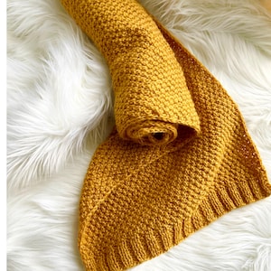 May include: A mustard yellow crocheted blanket with a textured stitch pattern. The blanket is rolled up and folded in half.