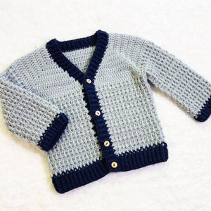 May include: A gray crocheted cardigan with a navy blue trim and wooden buttons.