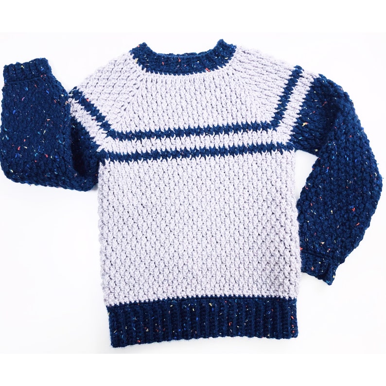 May include: A crocheted sweater with long sleeves in a light gray color with navy blue stripes and navy blue sleeves with flecks of color.