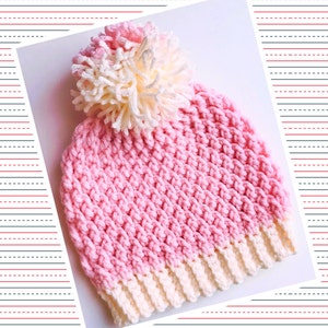 Può includere: Un berretto lavorato a uncinetto rosa e bianco con un pompon soffice in cima.