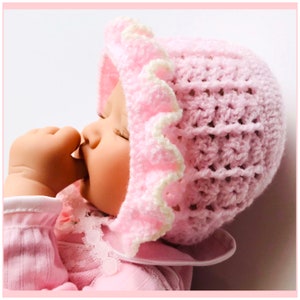May include: A pink crocheted baby hat with a white ruffle trim. The hat is made with a delicate stitch pattern and has a soft, cozy feel.
