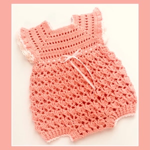 May include: A crocheted baby romper in a light pink colour with white trim and a white ribbon tied at the waist.