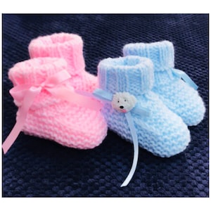 May include: A pair of knitted baby booties, one pink and one blue, with ribbon bows and a small white bear applique on the blue bootie.