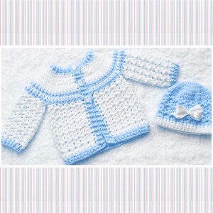 Puede incluir: Un c&aacute;rdigan de beb&eacute; de punto blanco y azul claro con cierre de bot&oacute;n y un gorro a juego de punto azul claro con un lazo blanco.