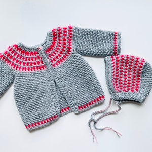 May include: A gray crocheted baby cardigan and matching hat with pink and red stripes. The cardigan has a button closure and the hat has a tie.
