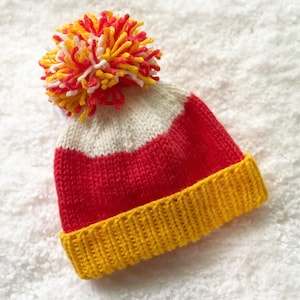 May include: A red, white, and yellow striped knitted hat with a pom-pom on top.