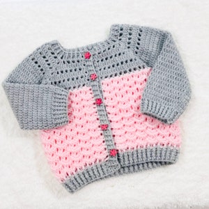 May include: A gray and pink crocheted baby cardigan with flower-shaped buttons.