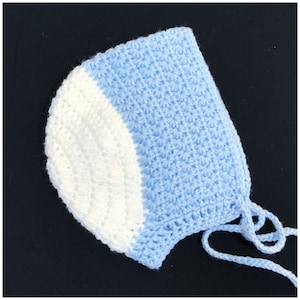 Peut inclure: Bonnet pour bébé fait à la main, en crochet bleu clair et blanc. Le bonnet présente un motif de point en forme d'étoile et des liens sous le menton. Les couleurs pastel sont douces.