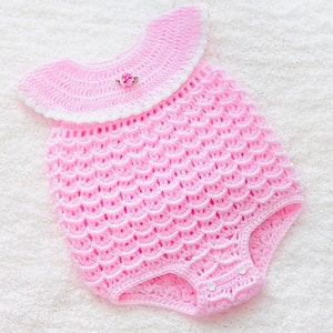 May include: A pink crocheted baby onesie with a white crocheted collar and a small pink flower embellishment.