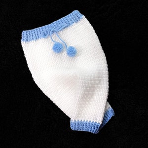 May include: White crocheted baby pants with blue trim and pom-poms.