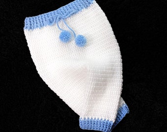 May include: White crocheted baby trousers with blue trim and pom-poms.