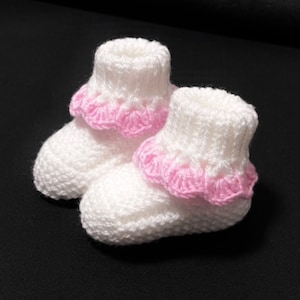 May include: A pair of white knitted baby booties with pink crocheted trim around the top.