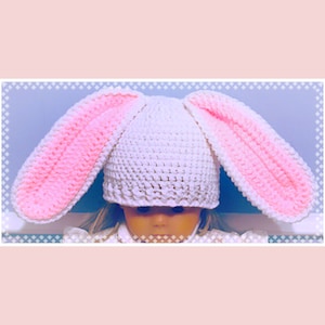 May include: White crocheted bunny hat with pink ears. The hat is made with a single crochet stitch and has a simple design.