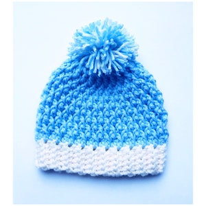 May include: A blue crocheted beanie with a white pom pom and a white crocheted brim.