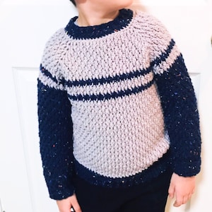 May include: A crocheted sweater with a light purple body and navy blue sleeves. The sweater has two horizontal stripes of navy blue across the chest.