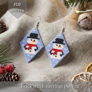 Könnte beinhalten: Ein Paar rautenförmige Brick-Stitch-Ohrringe mit einem Schneemann-Motiv, bestehend aus schwarzem Hut, orangefarbener Nase und rotem Schal auf hellblauem Grund, präsentiert mit einem PDF-Muster-Etikett und Text.