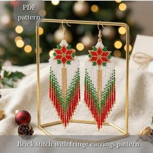 May include: A pair of beaded earrings featuring a white, red, and green geometric star design at the top with long, multi-colored fringe strands. The earrings are displayed on a gold metal stand. Text reads: PDF pattern and Brick stitch with fringe earrings pattern.
