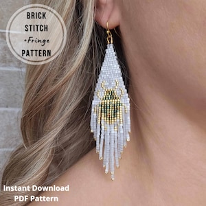 May include: A long, triangular beaded earring featuring a white background with a central beetle motif in metallic gold and dark green. The earring is constructed with a brick stitch and fringe pattern, hanging from a gold-toned metal hook.