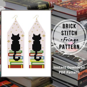 May include: A pair of long, triangular beaded earrings featuring a black cat silhouette sitting on a stack of colorful books. The background is a light pink grid pattern with small gold cross accents. The earrings hang from gold-toned metal hooks.