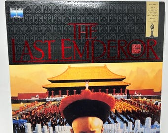 May include: A LaserVideodisc of the film "The Last Emperor". The cover displays the title in red, a photo of a young boy in traditional clothing, and a scene of a large crowd in front of a palace. The top section has a black background with a repeating pattern.