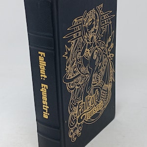 Op de afbeelding: Een zwart hardcover boek getiteld Fallout: Equestria met goudfolie op de voorkant en de rug. De voorkant bevat een gedetailleerde gouden lijnillustratie van een pony, terwijl de rug de titeltekst weergeeft.