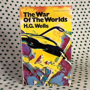 Puede incluir: Una portada de libro de bolsillo con fondo amarillo y una ilustración en blanco y negro de una nave espacial. El título del libro es "La guerra de los mundos" de H.G. Wells. El libro está publicado por Scholastic.
