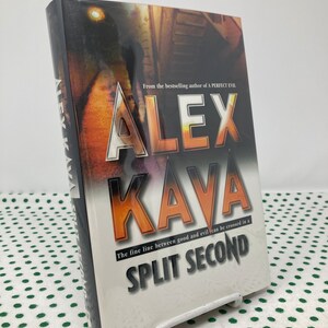 May include: A white book cover with a dark image of a person walking down a dark alley. The title of the book is "ALEX KAYA" in large, bold, orange letters. The subtitle is "The fine line between good and evil can be crossed in a SPLIT SECOND".