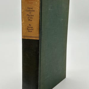Puede incluir: Un libro antiguo de tapa dura titulado "Heartbreak House, Great Catherine & Playlets of the War" de George Bernard Shaw. El libro tiene una cubierta verde oscuro y una etiqueta marrón con texto negro.