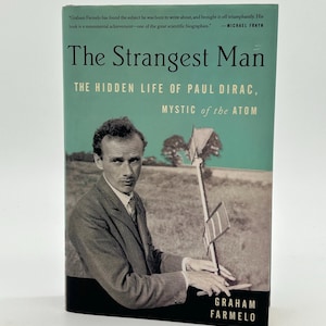 May include: A book titled "The Strangest Man" with a teal and black cover. The cover features a black and white photo of a man in a suit holding a scientific instrument. The author's name, Graham Farmelo, is printed at the bottom.