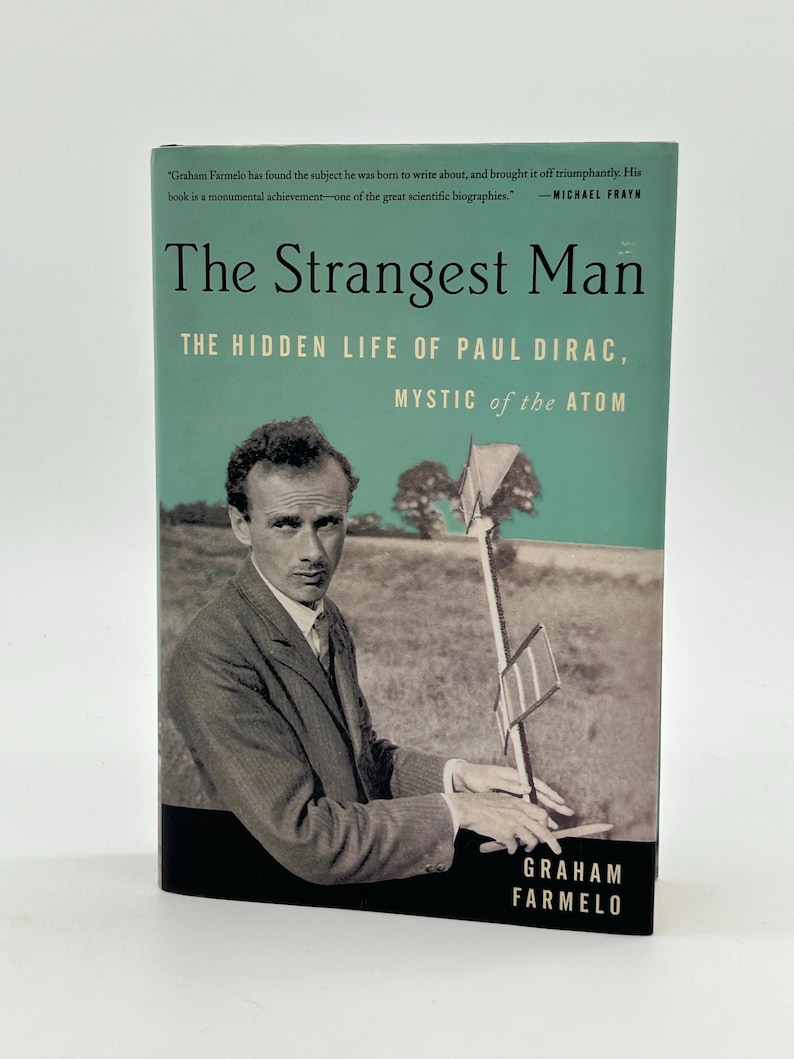 May include: A book titled "The Strangest Man" with a teal and black cover. The cover features a black and white photo of a man in a suit holding a scientific instrument. The author's name, Graham Farmelo, is printed at the bottom.