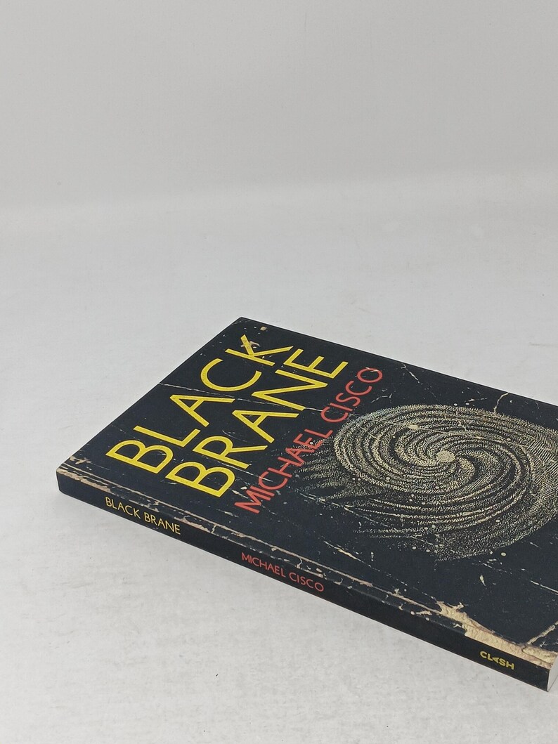 Puede incluir: Un libro de bolsillo titulado Black Brane de Michael Cisco. La portada es negra con un gr&aacute;fico de espiral amarillo, texto amarillo para el t&iacute;tulo y texto rojo para el nombre del autor. El lomo tambi&eacute;n muestra el t&iacute;tulo, el autor y la editorial Clash.