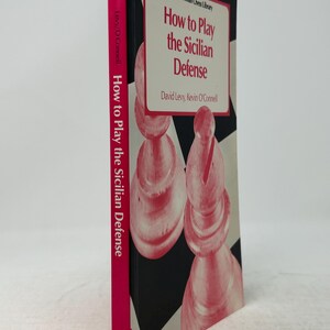 K&ouml;nnte beinhalten: Ein Buch mit dem Titel "How to Play the Sicilian Defense" von David Levy und Kevin O'Connell. Das Buch hat einen pinkfarbenen Buchr&uuml;cken mit dem Titel und dem Namen des Autors. Das Cover zeigt Schachfiguren in Rosa und Wei&szlig;, mit dem Titel in Rot.