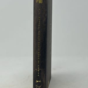 Puede incluir: Un libro marr&oacute;n oscuro titulado "Little Black Book of Stories" de A.S. Byatt. El lomo del libro presenta letras doradas y detalles florales dorados decorativos en la parte superior e inferior. El libro est&aacute; de pie sobre un fondo blanco.
