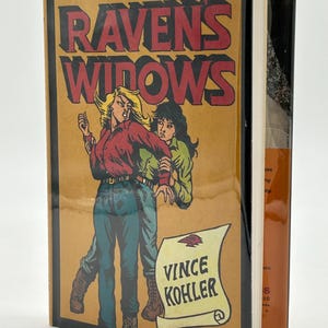 May include: A vintage paperback book titled "Raven's Widows" by Vince Kohler. The cover features a retro illustration of two women in a dramatic pose, set against a tan background. The book is part of "An Eldon Larkin Mystery" series.