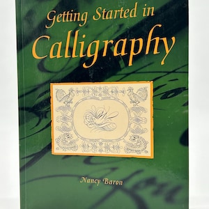 以下が含まれることがあります： 緑色の背景にオレンジ色のタイトルで「Getting Started in Calligraphy」というタイトルの本。表紙には、カリグラフィーと著者の名前であるナンシー・バロンが描かれた、装飾的で額縁に入ったイラストが描かれています。