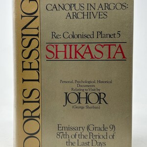May include: A hardcover book titled "Canopus in Argos: Archives" by Doris Lessing. The book's cover is tan with black and red text, including "Shikasta" in large red letters. The book also includes the text "Re: Colonised Planet 5".