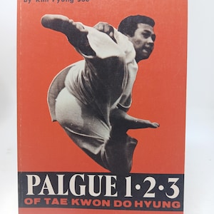 Puede incluir: Portada de libro con fondo rojo e imagen en blanco y negro de un hombre en postura de Tae Kwon Do. El título "PALGUE 1·2·3" está en blanco sobre una banda negra, con "OF TAE KWON DO HYUNG" debajo. El nombre del autor, "by Kim Pyung Soo", está en la parte superior.