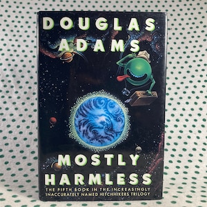 Könnte beinhalten: Ein Buchcover mit schwarzem Hintergrund und einem blauen und grünen Planeten in der Mitte. Der Titel "MOSTLY HARMLESS" ist in weißen Buchstaben geschrieben. Der Name des Autors, "DOUGLAS ADAMS", ist in weißen Buchstaben über dem Planeten geschrieben. Der Text "THE FIFTH BOOK IN THE INCREASINGLY INACCURATELY NAMED HITCHHIKERS TRILOGY" ist in weißen Buchstaben unter dem Planeten geschrieben.