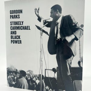 May include: Black and white photograph of a book cover featuring a man speaking into a microphone. The book title reads "GORDON PARKS STOKELY CARMICHAEL AND BLACK POWER". The image shows a crowd of people in the background.