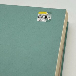 May include: A teal-colored book with a textured cover. A sticker on the cover reads "Good" above a barcode and the price "$6.9". The book's pages are visible on the right side.