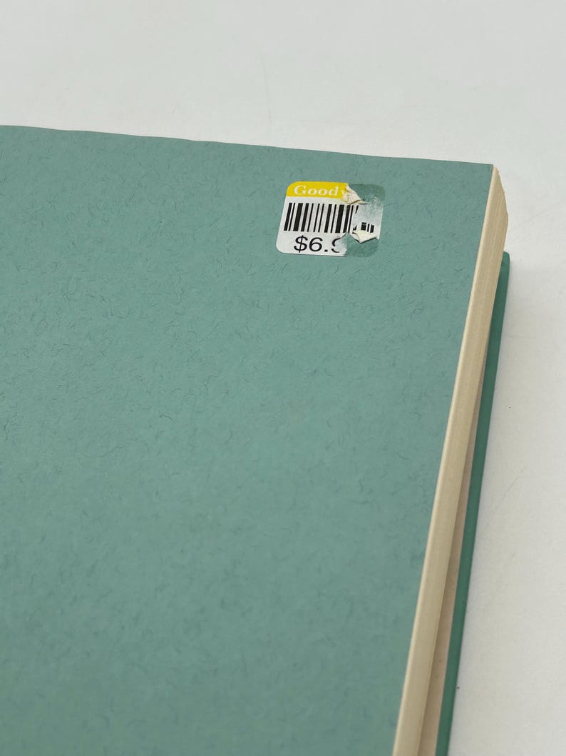 May include: A teal-colored book with a textured cover. A sticker on the cover reads "Good" above a barcode and the price "$6.9". The book's pages are visible on the right side.