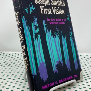May include: A black book with a purple and teal illustration of a forest on the cover. The title is "Joseph Smith's First Vision" and the subtitle is "The First Vision in its historical context". The author is Milton V. Backman, Jr.