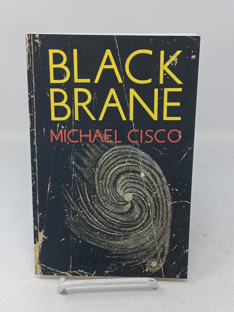 Puede incluir: Un libro de bolsillo titulado Black Brane de Michael Cisco. La portada es negra con el t&iacute;tulo en amarillo y el autor en naranja. Un gr&aacute;fico blanco en forma de espiral arremolinada que recuerda a una galaxia est&aacute; centrado en la parte inferior.