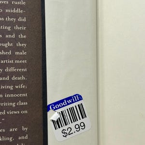 Puede incluir: Un libro con una p&aacute;gina blanca y una p&aacute;gina marr&oacute;n. Una pegatina azul y blanca de Goodwill est&aacute; adherida al libro. La pegatina tiene un c&oacute;digo de barras y el texto "Goodwill" y "$2.99".
