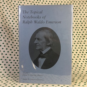 May include: The cover of a blue book titled "The Topical Notebooks of Ralph Waldo Emerson" with a black and white portrait of Ralph Waldo Emerson. The book is volume 3, edited by Glen M. Johnson and Ralph H. Orth, Chief Editor.