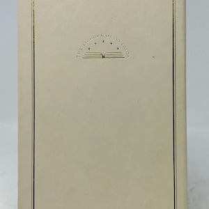 Pode incluir: Um livro retangular com uma capa creme. A capa apresenta uma borda dourada e as palavras "THE LIBRARY OF AMERICA" acima de uma ilustração de um livro aberto. O design do livro é simples e elegante.